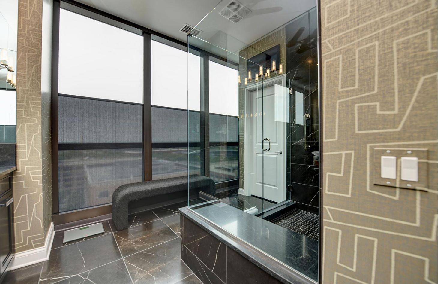 A contemporary bathroom with a black marble shower, large windows, and partially drawn shades for privacy.