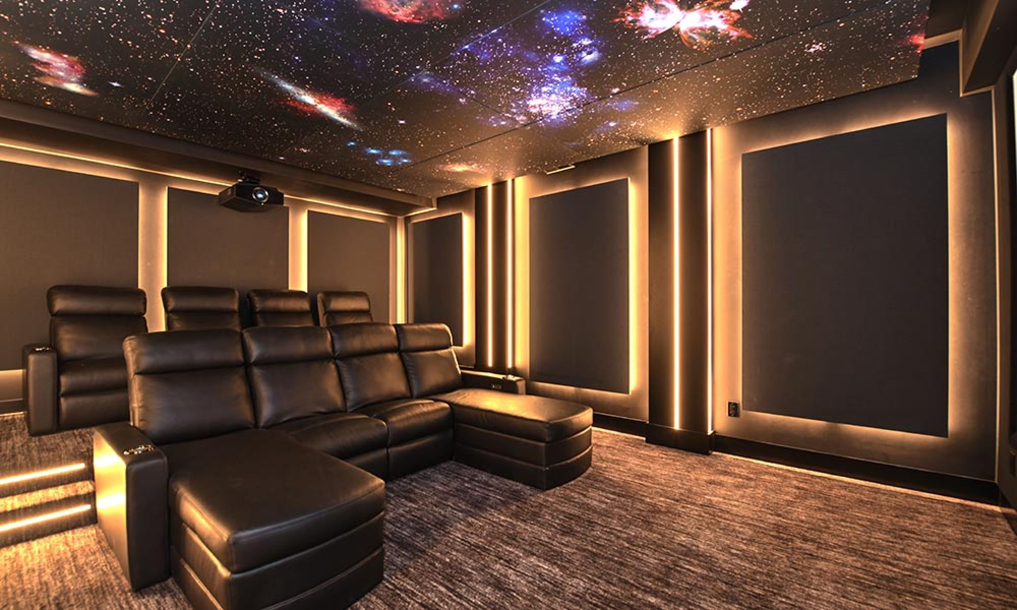 A luxurious home theater room with reclining leather seats, ambient lighting, and a ceiling adorned with a galaxy-themed design.