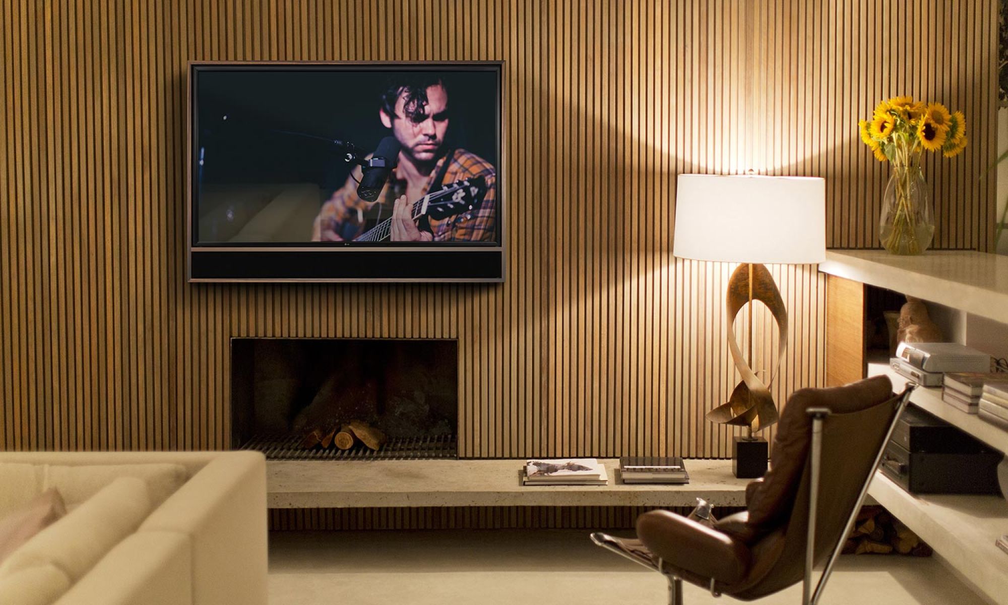 A modern living room with a wooden accent wall, a flat-screen TV showing a musician, and a Leon soundbar.