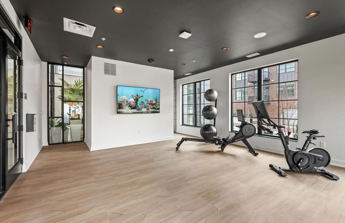 Minimalist fitness room with exercise equipment, large windows, and a wall-mounted fish tank display.