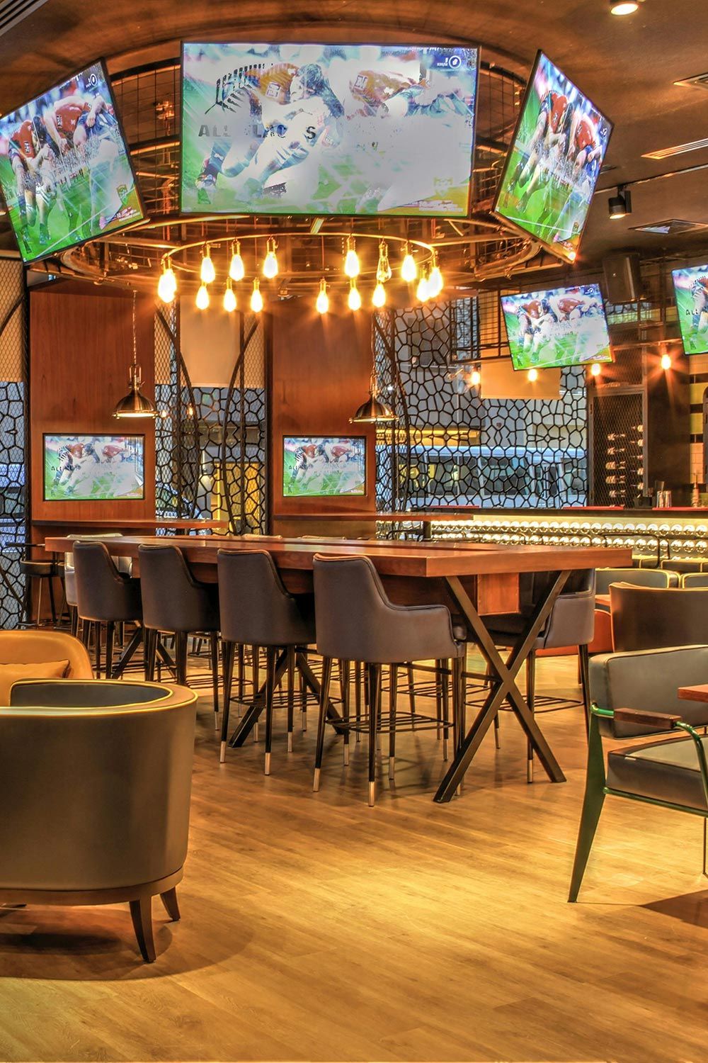 Modern sports bar with multiple large screens, stylish decor, and high-top seating.