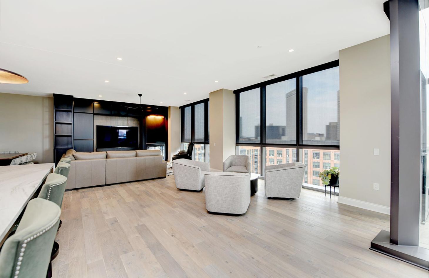 A living room with a light beige sectional, black ceiling fan, and large floor-to-ceiling windows showcasing an urban skyline.