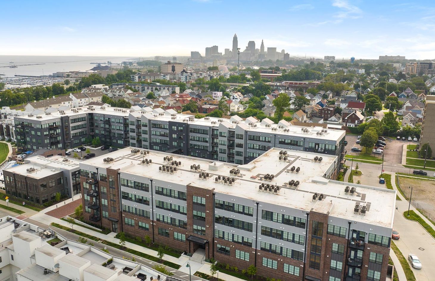 Aerial view of a large residential complex with a city skyline in the background near a waterfront.