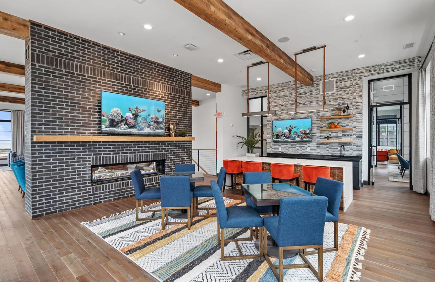 Stylish dining and kitchen area with a mix of blue and orange seating, wooden beams, and contemporary lighting.