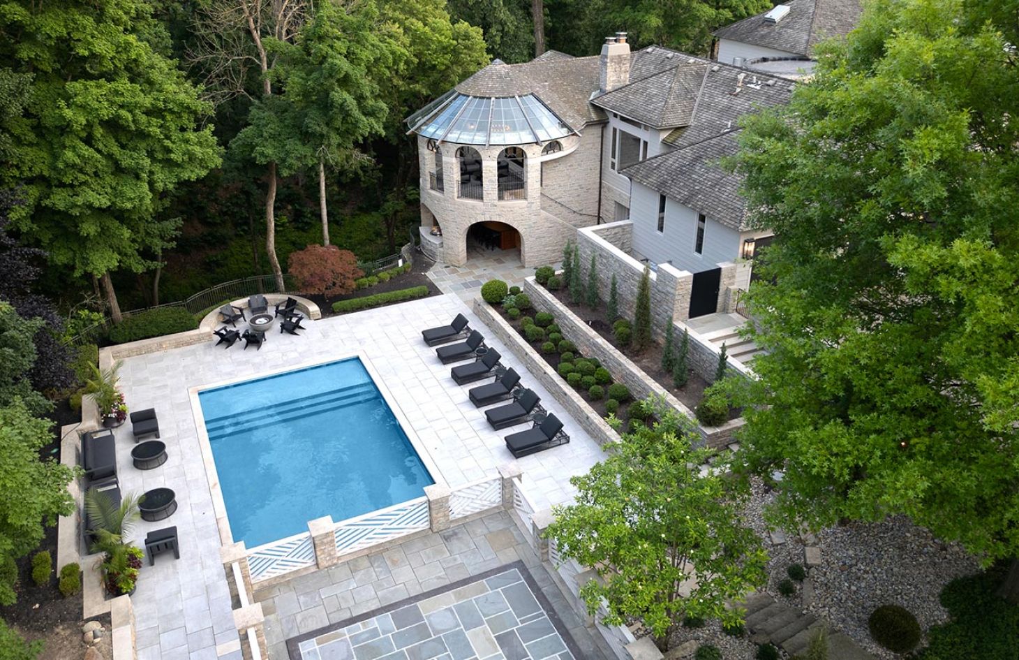 An aerial view of a house with a pool, lounge chairs, and a rounded tower surrounded by trees.