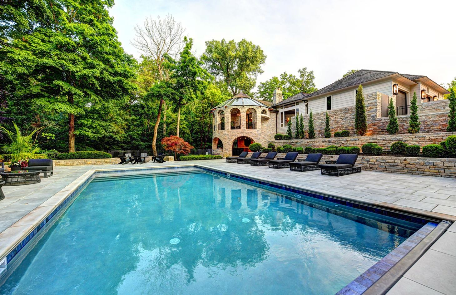 A spacious outdoor pool area with surrounding lounge chairs and lush greenery.