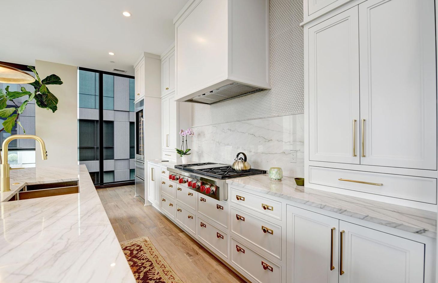 A sleek kitchen featuring white cabinets, a marble countertop, and a stainless steel refrigerator with a modern, bright design.