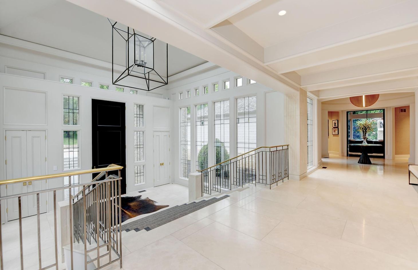 A grand entrance hall with high ceilings, a statement chandelier, and a modern staircase leading to upper and lower levels.