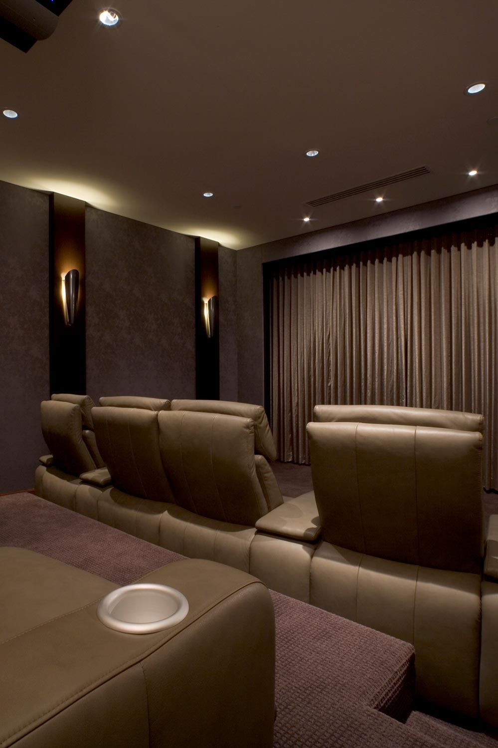 A dimly lit home theater room with brown leather recliner seats and wall sconces providing soft lighting.