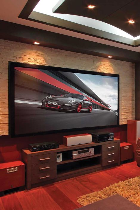 A home theater setup with a large screen displaying a racing car, a stylish entertainment center with audio equipment, and a warm-toned decor.