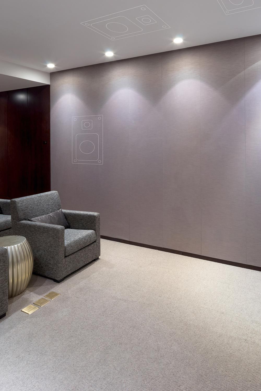 A home theater with grey seating, wall and ceiling-mounted Sonance speakers indicated by outlines on the walls.