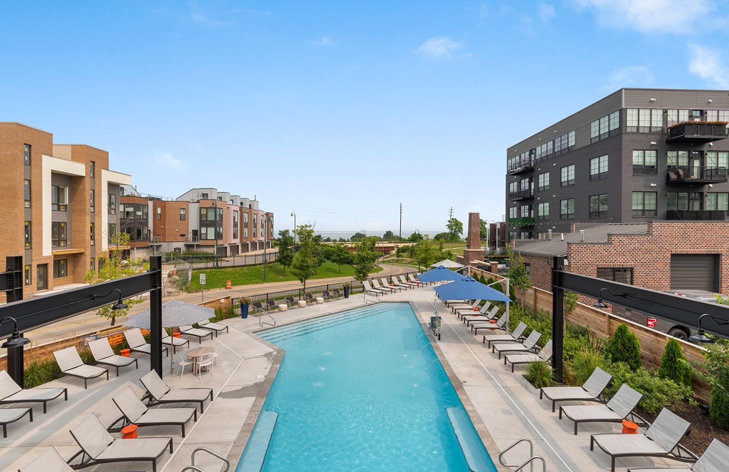 Outdoor pool area surrounded by lounge chairs, shaded umbrellas, and views of modern residential buildings.