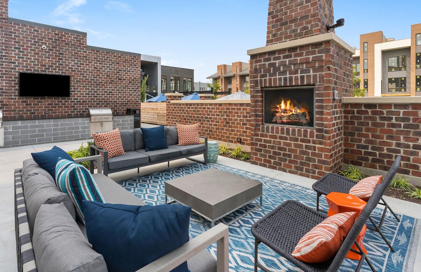 Outdoor seating area with a brick fireplace, comfortable sofas, colorful pillows, and a cozy atmosphere.