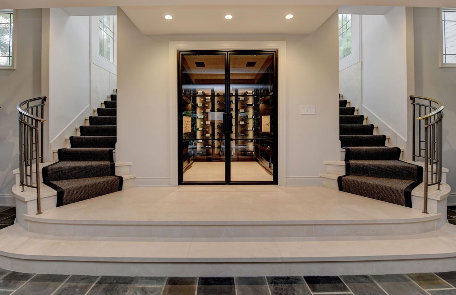 A stylish wine storage room with a glass door, flanked by elegant carpeted staircases.