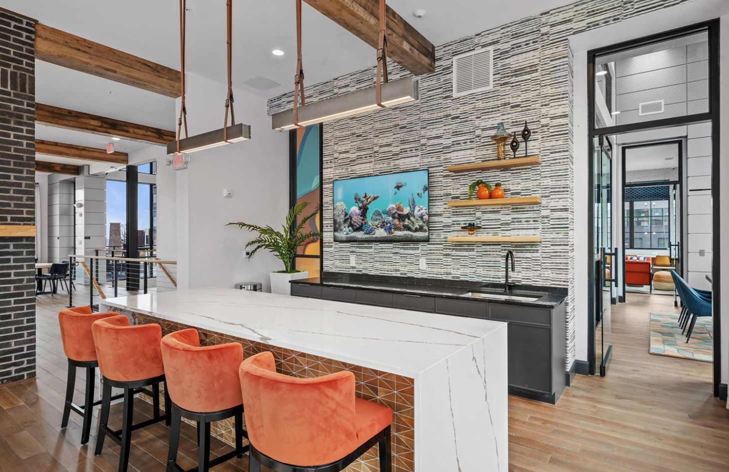 Modern kitchen with a large island, orange bar stools, open shelving, and a fish tank display on the wall.