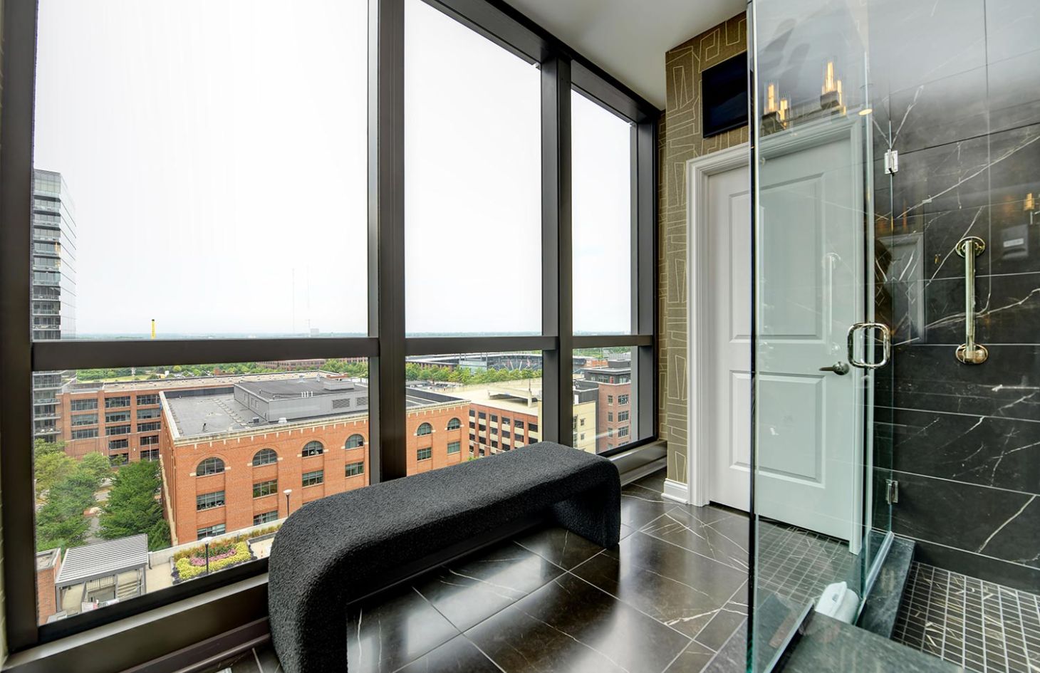 A modern bathroom with a glass shower, black marble floor, and expansive windows providing ample natural light.