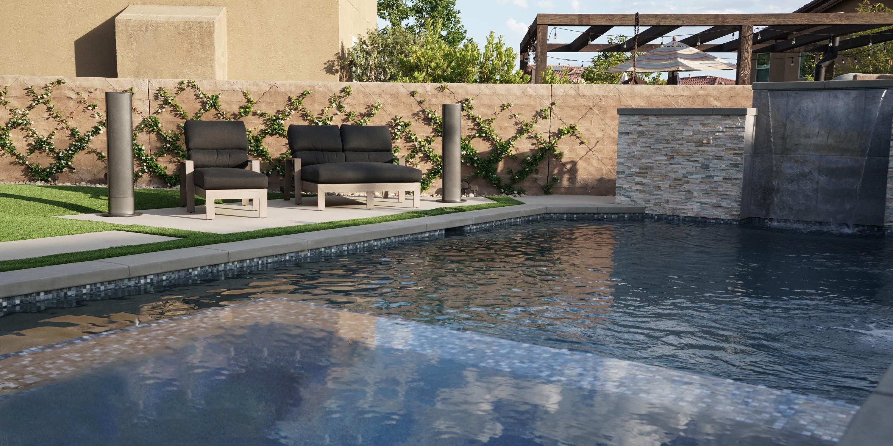 Outdoor pool area with modern lounge chairs and a decorative stone wall featuring a water fountain.