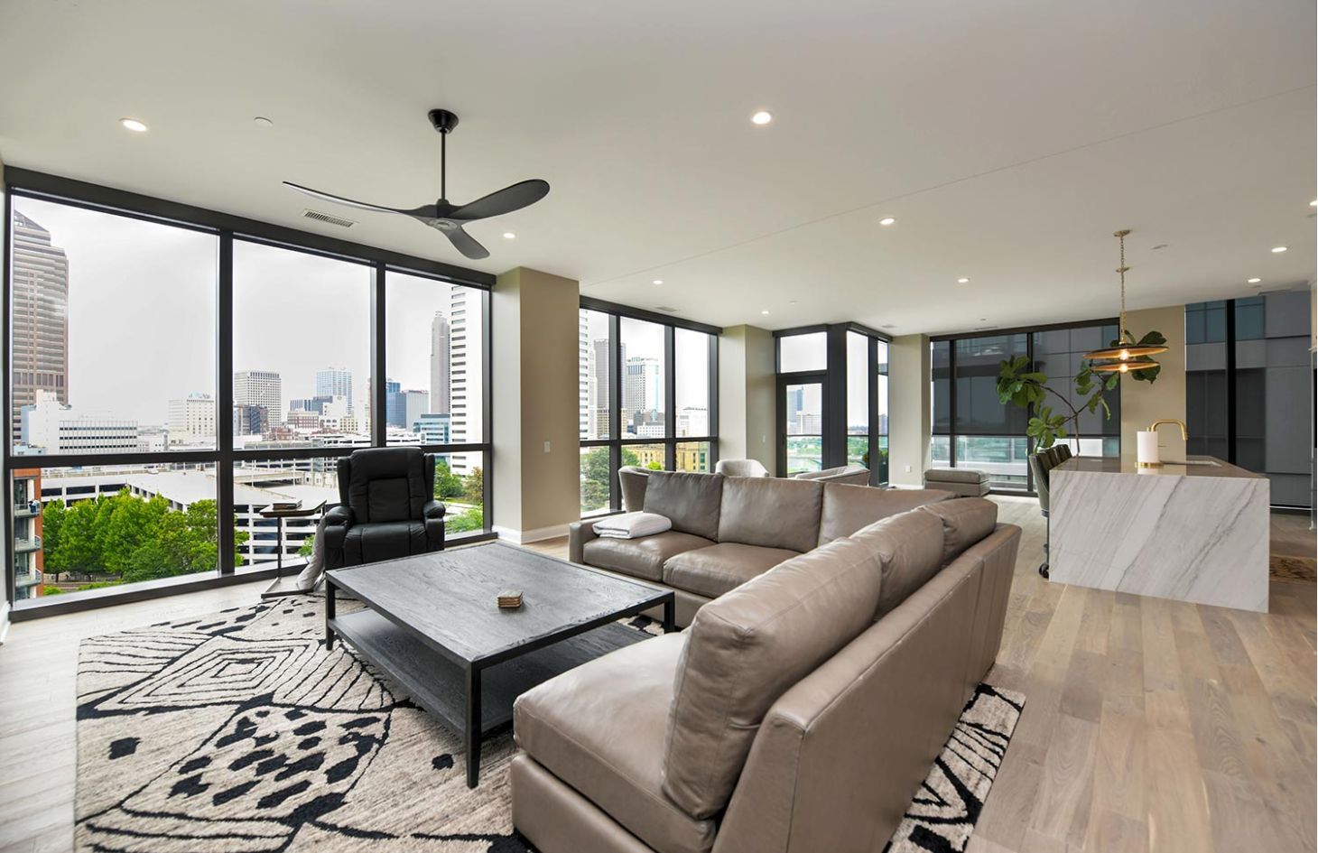 A cozy living area featuring a large sectional, black armchair, and floor-to-ceiling windows overlooking city buildings.