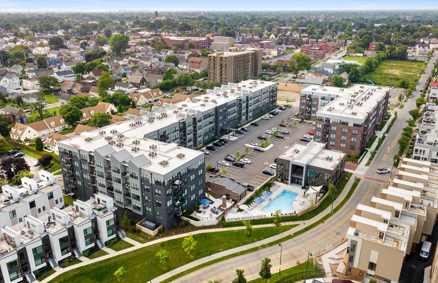 Elevated view of a residential area with contemporary apartment buildings, parking lot, and outdoor pool.