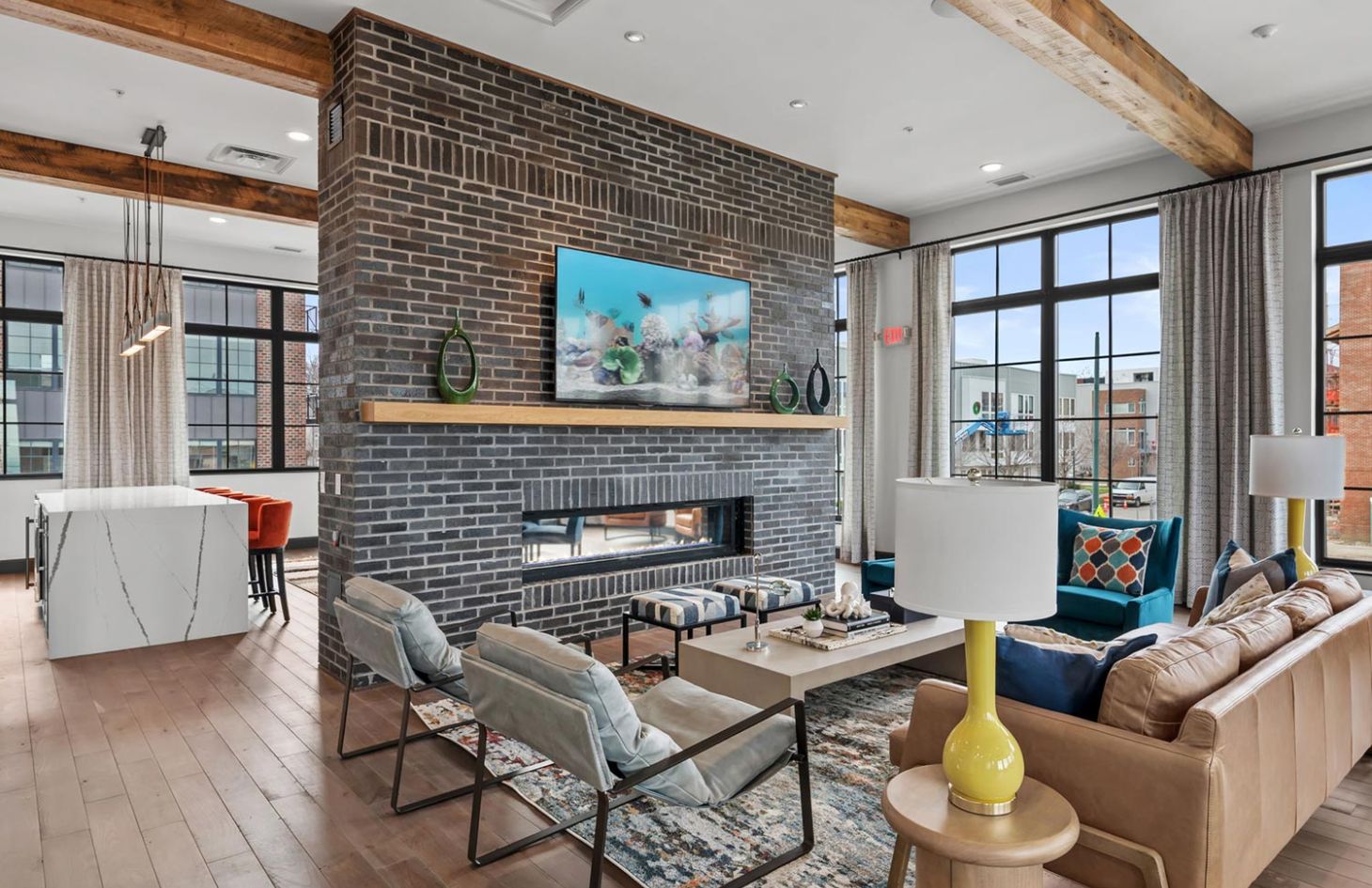 Cozy lounge area with modern seating, large windows, and a double-sided brick fireplace with a mounted fish tank display.