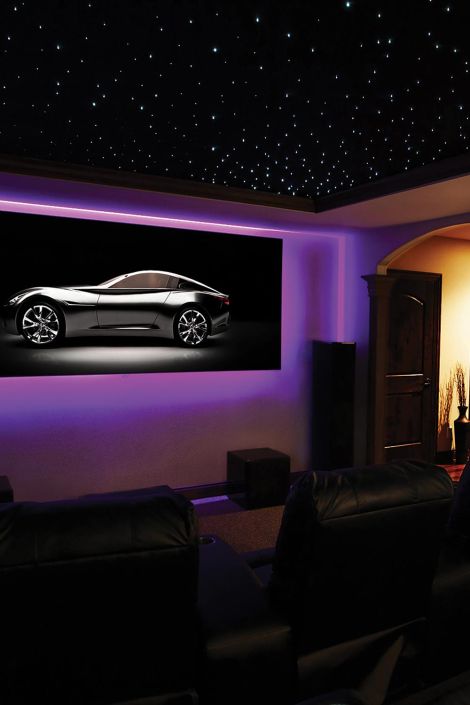 A home theater with a large screen showing a sleek black car, ambient purple lighting, and a starry ceiling with comfortable seating.