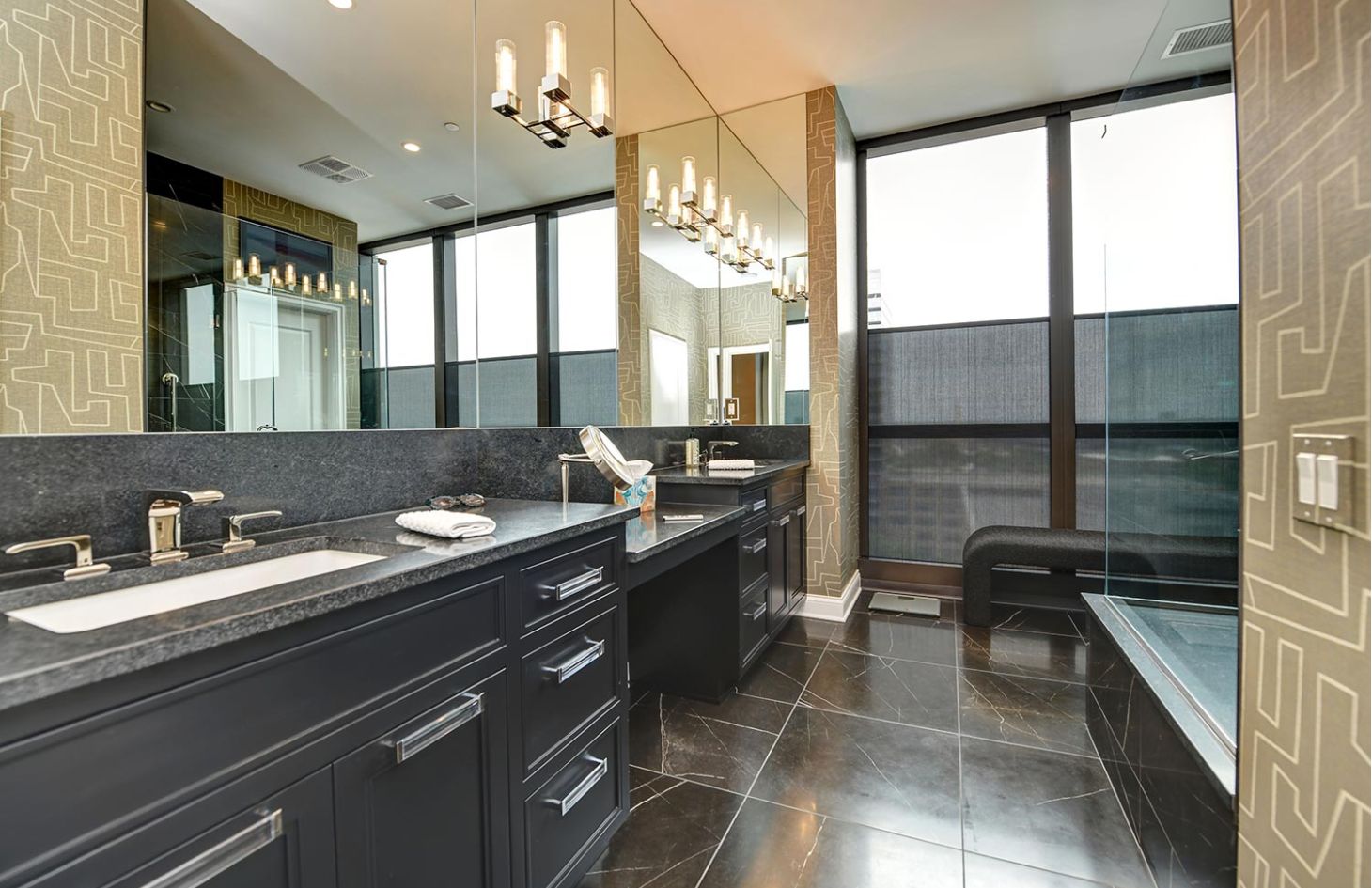 A contemporary bathroom featuring black cabinetry, a large mirror, and partially drawn shades over floor-to-ceiling windows.