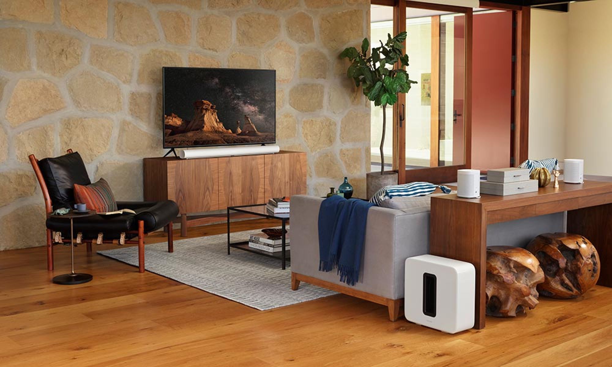 A TV on a white entertainment unit displaying a colorful graphic with a Sonos soundbard and modern decor items around it.