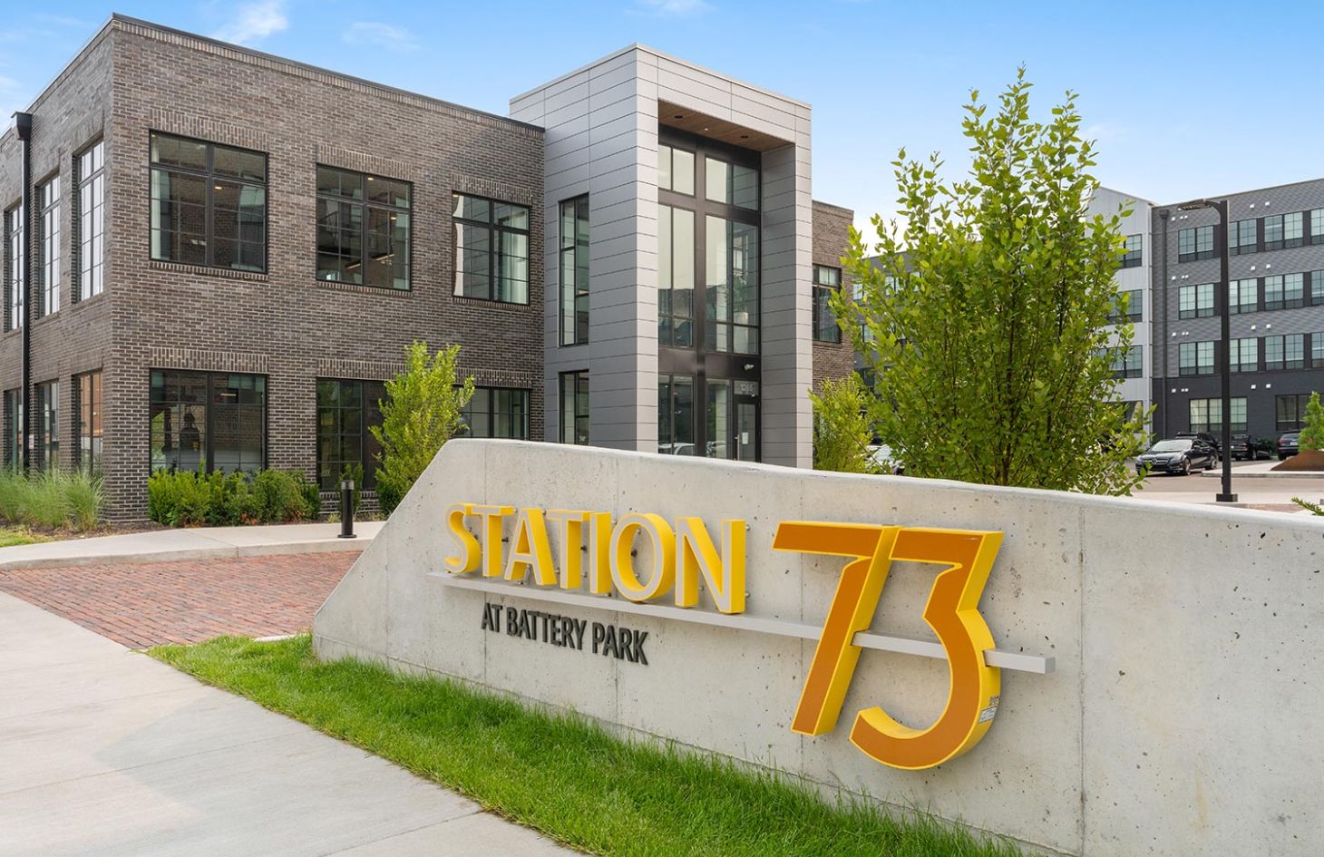 Modern building with large windows, surrounded by greenery, featuring a bold yellow sign reading "Station 73".