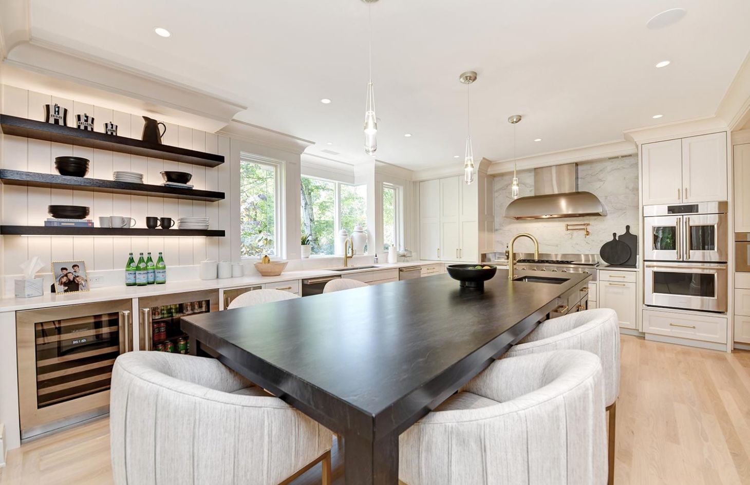 A bright kitchen with a large island, open shelving, and stainless steel appliances, featuring pendant lighting and a clean, modern design.